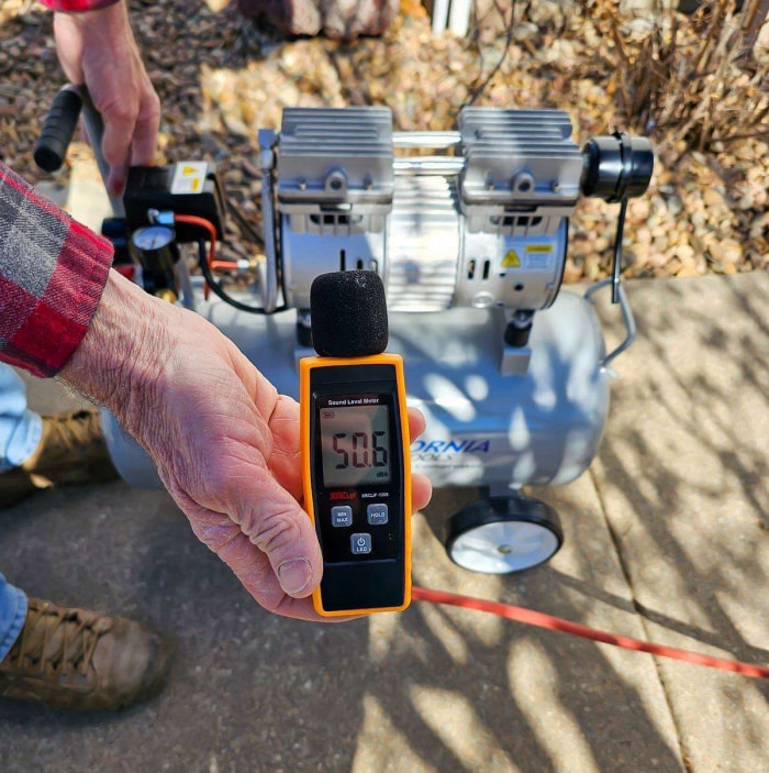 Une personne tenant un décibelmètre indiquant 50,6 à côté du compresseur d'air California Air Tools 8010 pendant les tests.