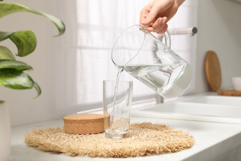 Une femme verse de l'eau dans un verre à partir d'une cruche en verre sur le comptoir de la cuisine.