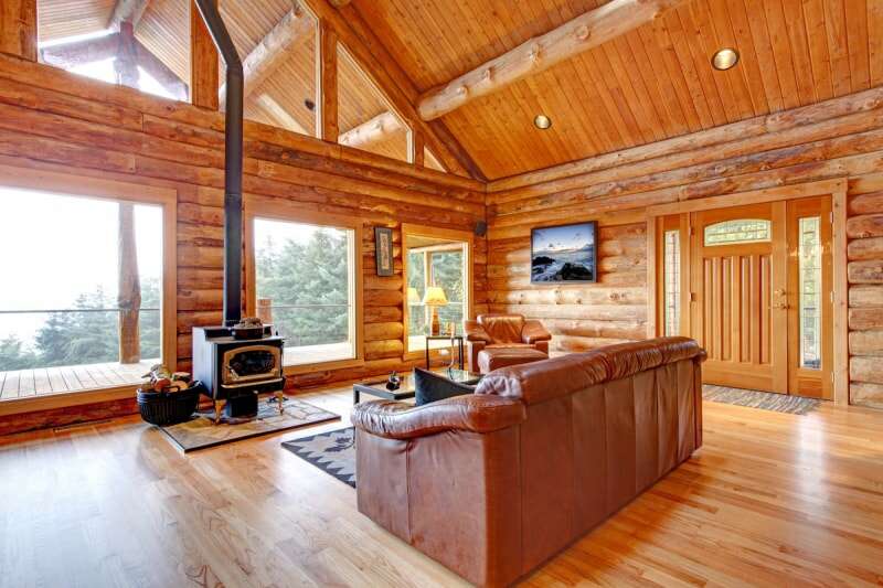 L'intérieur du salon d'une cabane en rondins de luxe comprend du parquet, un canapé en cuir et un petit poêle à bois.