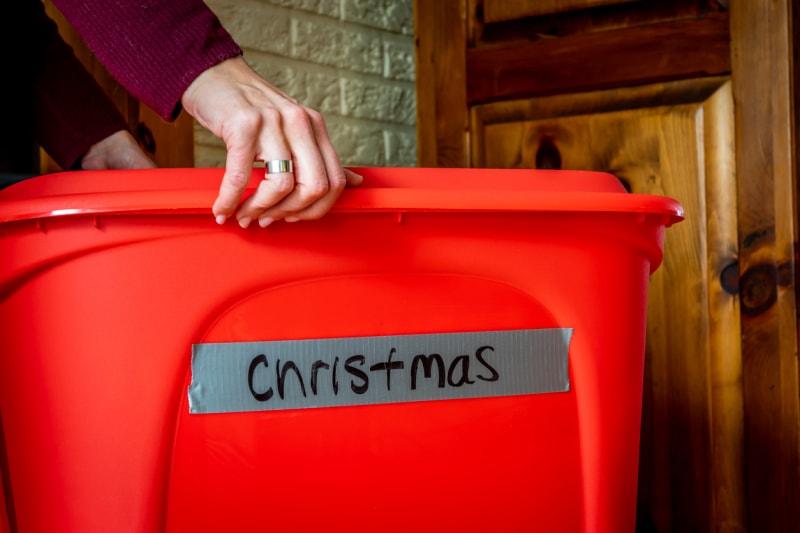 Femme ouvrant une boîte de rangement remplie de décorations de Noël pour la période des fêtes.