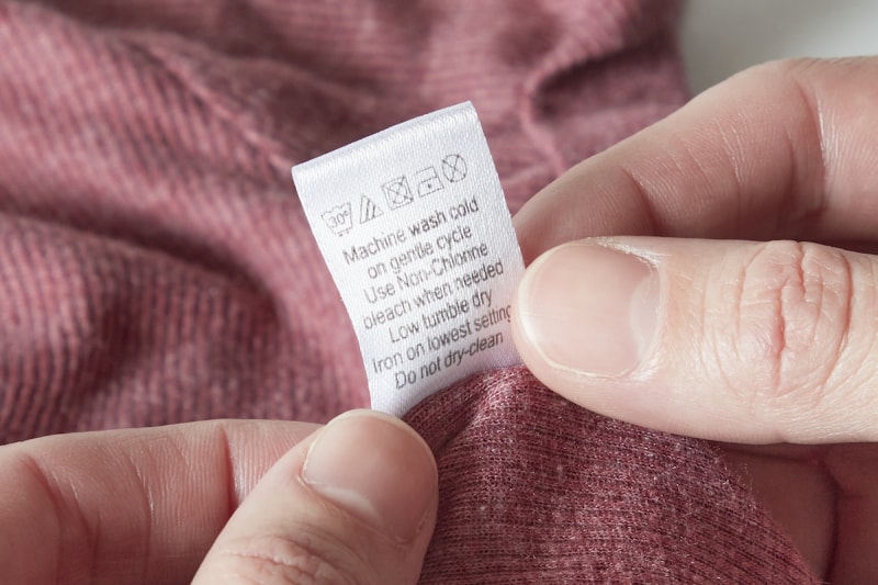 Une femme consulte le dos d'une étiquette de linge sur un t-shirt.