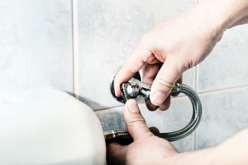 Une personne ferme le robinet d'eau des toilettes. 