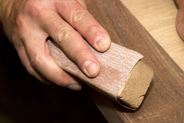 Gros plan d'un homme ponçant du bois à la main dans l'atelier.