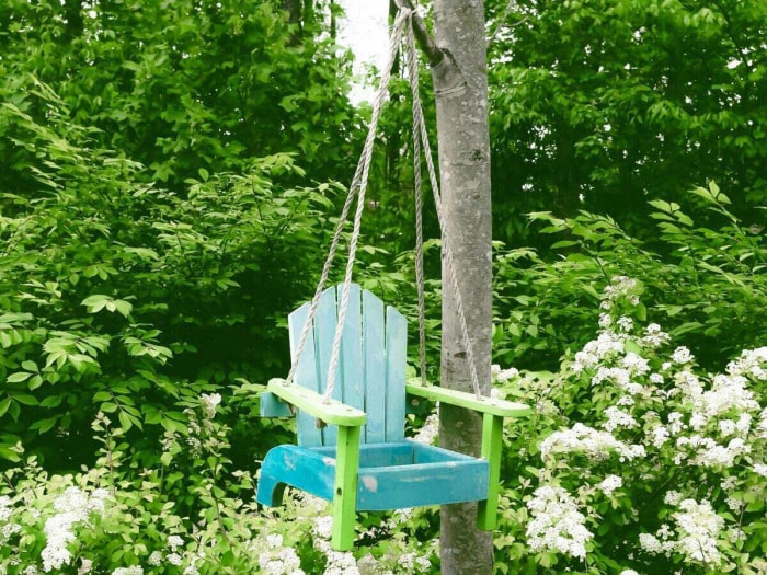 Une vieille chaise transformée en balançoire est suspendue à un arbre.