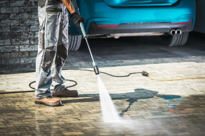 Lavage à pression d'une allée pavée par un travailleur caucasien.