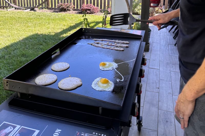 Personne cuisinant des crêpes, des œufs et du bacon sur une plaque chauffante Blackstone de 36 pouces dans l'arrière-cour.