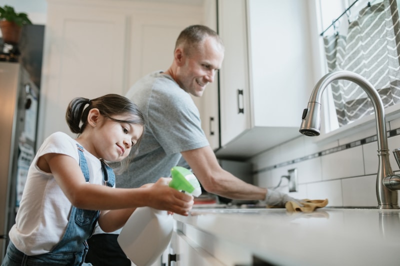 Père et fille désinfectant ensemble les surfaces de la cuisine