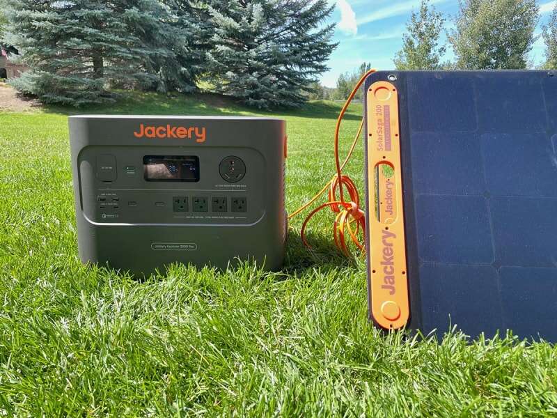 Le générateur solaire Jackery 3000 Pro connecté à ses panneaux solaires pour se recharger dans une cour ensoleillée