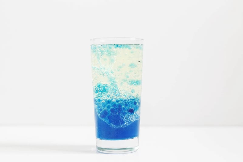 Un verre sur fond blanc avec une lampe Laval bleue faite maison à l'intérieur.