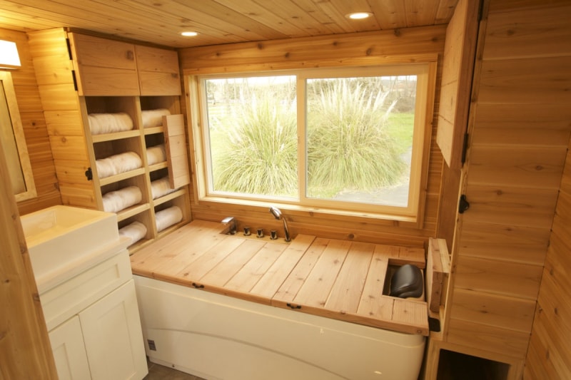 La salle de bain dans une petite maison avec des panneaux en bois de style sauna et un combo couvre-baignoire-banc.