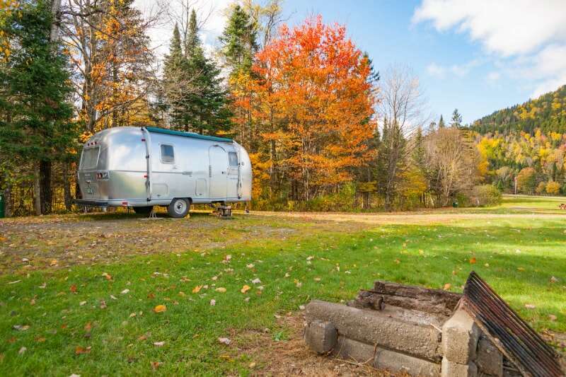 Une caravane Airstream est située devant des arbres devenant orange.