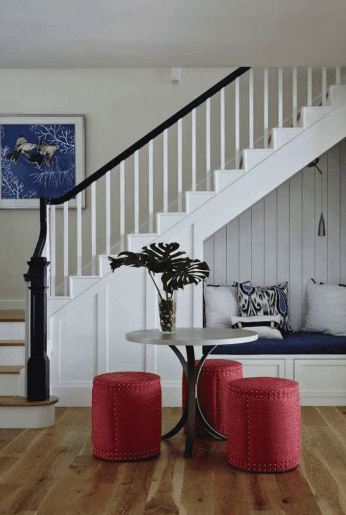 entrée vue de l'escalier avec une banquette rembourrée à l'intérieur d'un coin derrière une table ronde avec des tabourets cylindriques rouges