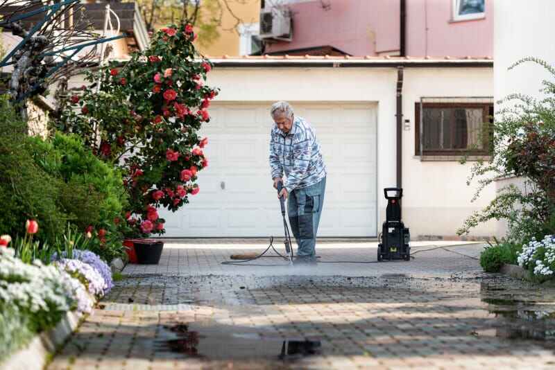 Un homme nettoie son allée avec un nettoyeur haute pression