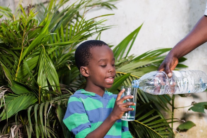 Un garçon se fait servir un verre d'eau à l'extérieur par une chaude journée d'été.