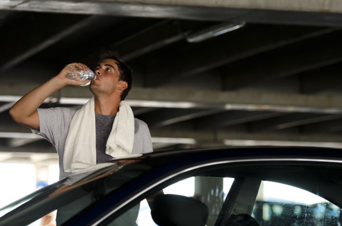 homme debout à l'extérieur de sa voiture se rafraîchissant avec une serviette et une bouteille d'eau