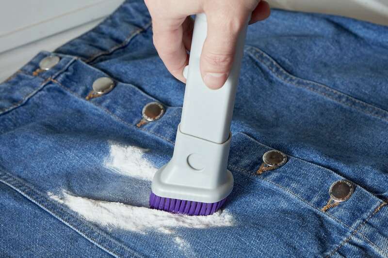 Une femme utilise une petite brosse à récurer pour éliminer le bicarbonate de soude d'une tache sur une jupe en jean.