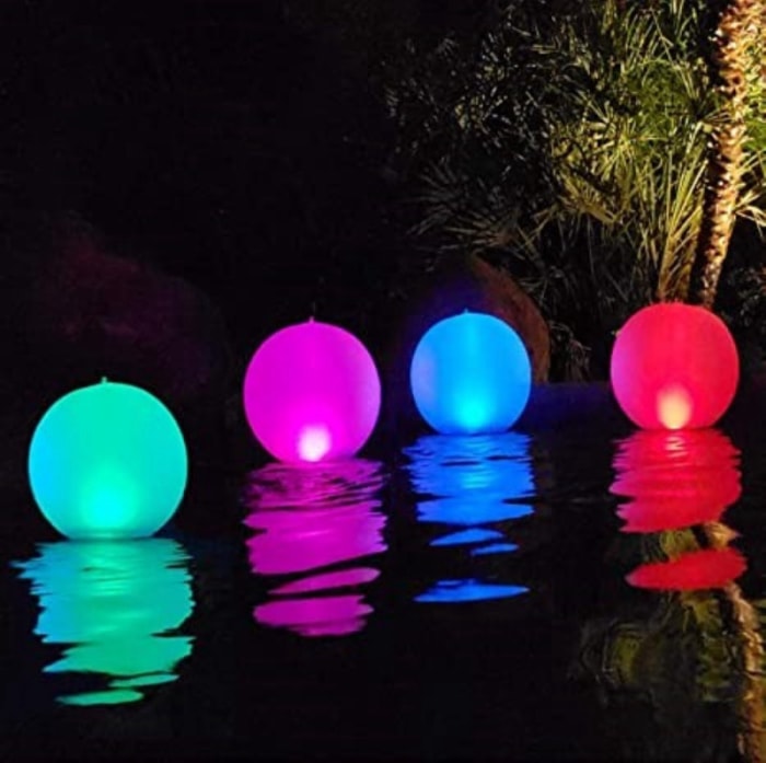 Une piscine la nuit éclairée par des globes lumineux flottants multicolores.