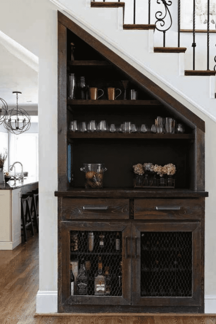 vue d'un meuble en bois foncé et d'un mini bar sous un élégant escalier dans un salon à aire ouverte