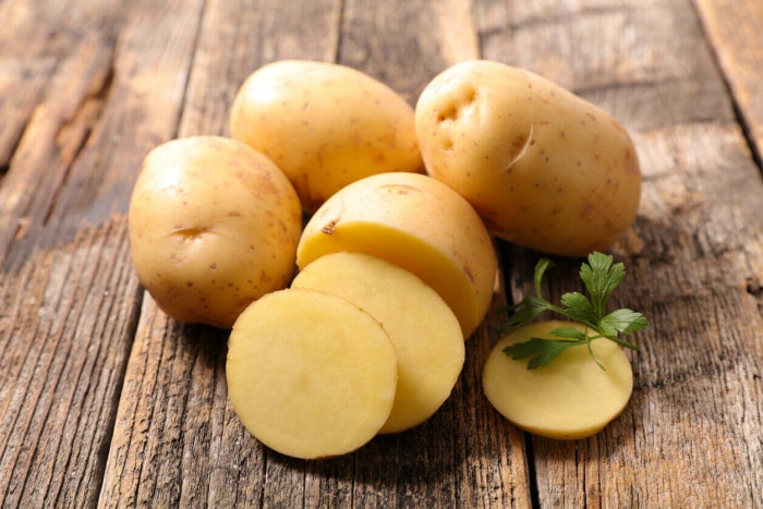 Pomme de terre partiellement coupée en rondelles entourée de pommes de terre entières et d'un brin de persil