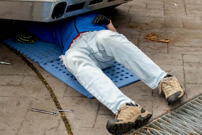 Un homme effectue des réparations sous une voiture, allongé sur un tapis rembourré