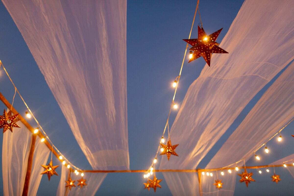 Des lanternes étoilées sont suspendues avec des guirlandes lumineuses dans le ciel du soir avec des draperies.