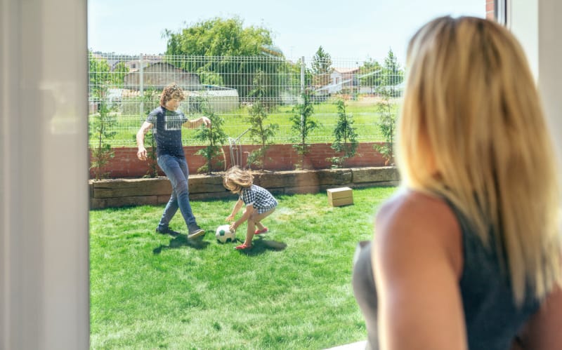 Une mère regarde son mari et son fils jouer au football dans le jardin