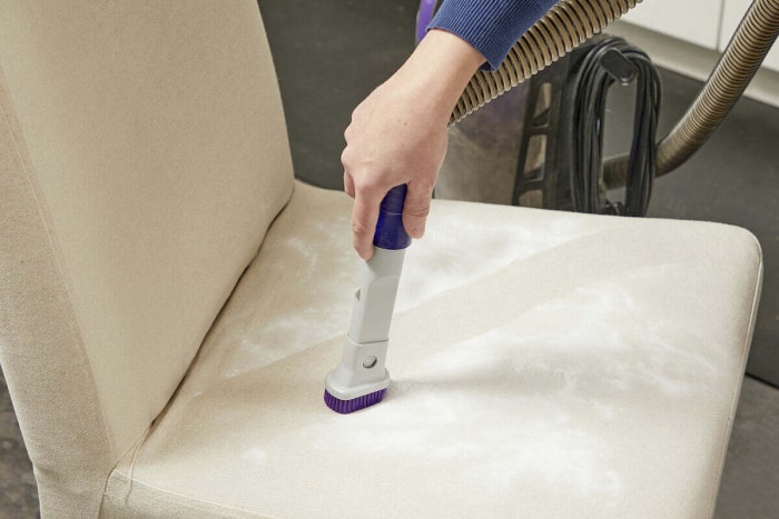 Une femme utilise un aspirateur pour enlever le bicarbonate de soude de l'assise d'une chaise.