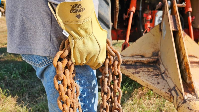 Personne portant des gants de travail en peau de chèvre jaune du Vermont tenant une chaîne rouillée