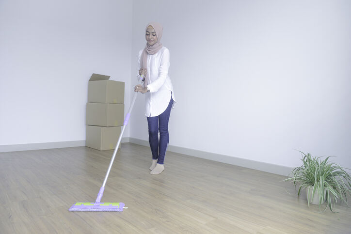 pièce vide avec femme en hijab beige et chemise blanche avec jeans nettoyant le sol avec swiffer et boîtes à proximité