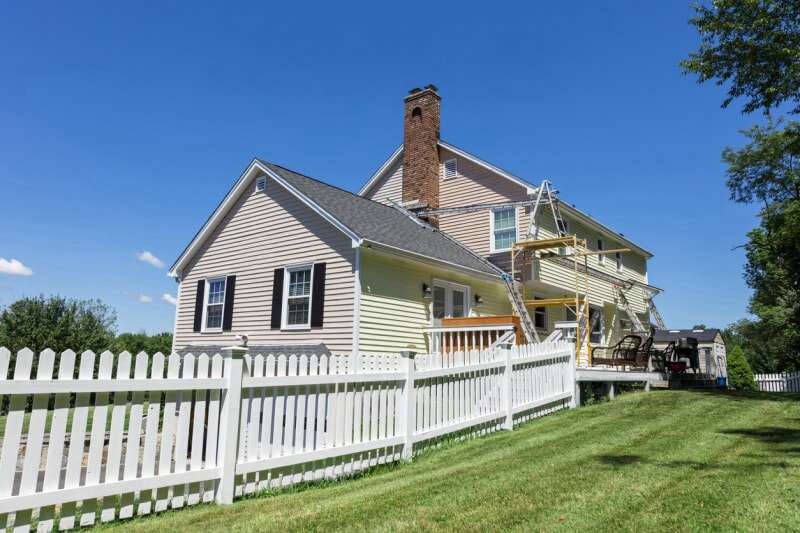 grande maison sur une pelouse verte avec un côté peint en beige et l'autre en jaune avec des échelles installées indiquant un travail de peinture