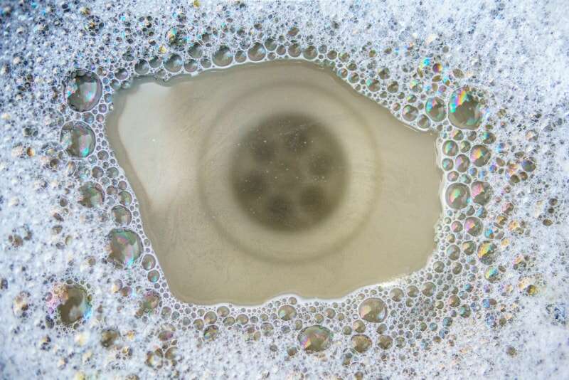 Vue rapprochée d'un drain d'évier sous de l'eau savonneuse qui s'est accumulée parce que le drain est bouché.