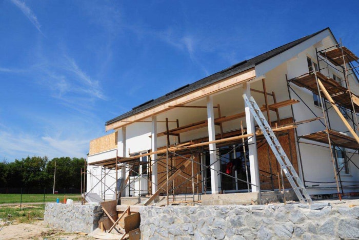 Une extension de maison est en cours de construction à l'arrière d'une maison, tandis que le côté de la maison est couvert par un échafaudage.