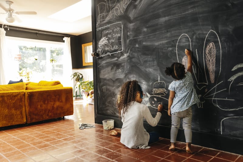 Deux enfants dessinent sur un mur transformé en tableau noir à la maison