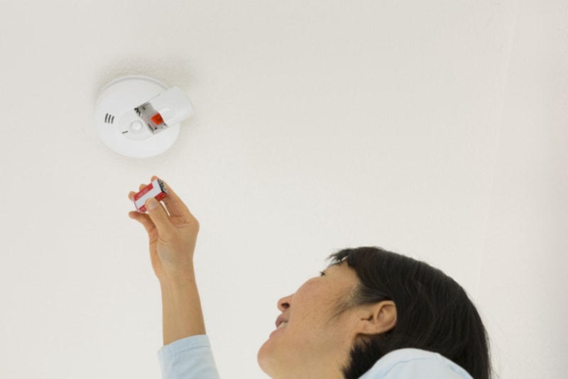 une femme s'approche pour changer la pile d'un détecteur de fumée sur un plafond blanc