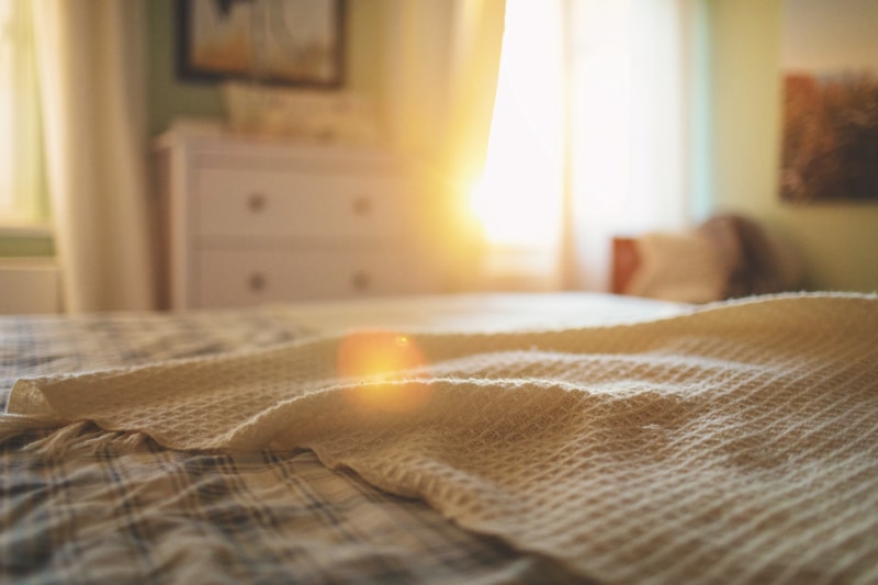 chambre à coucher avec lit au premier plan et lumière du soleil à travers la fenêtre