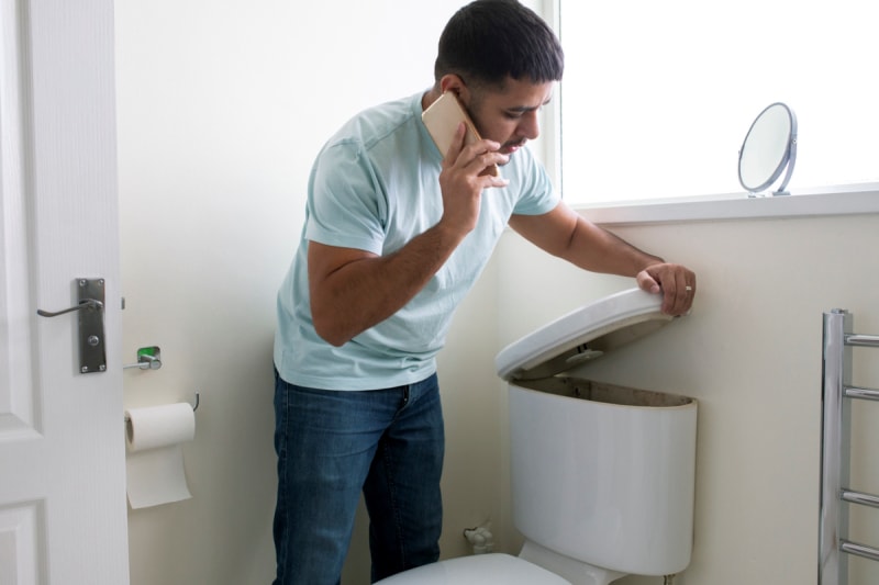 Homme au téléphone ouvrant le réservoir des toilettes