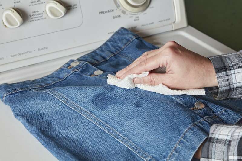 Une femme utilise une serviette en papier pour éponger une tache d’huile sur une jupe en jean.