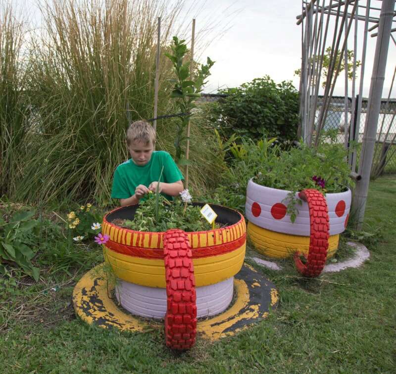 Un enfant travaille avec des plantes dans une jardinière faite de pneus peints.