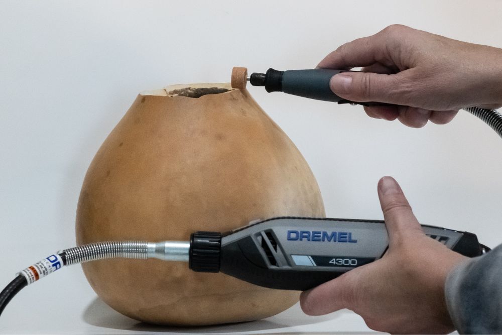 Personne utilisant Dremel 4300 pour couper le dessus d'une courge brun clair séchée