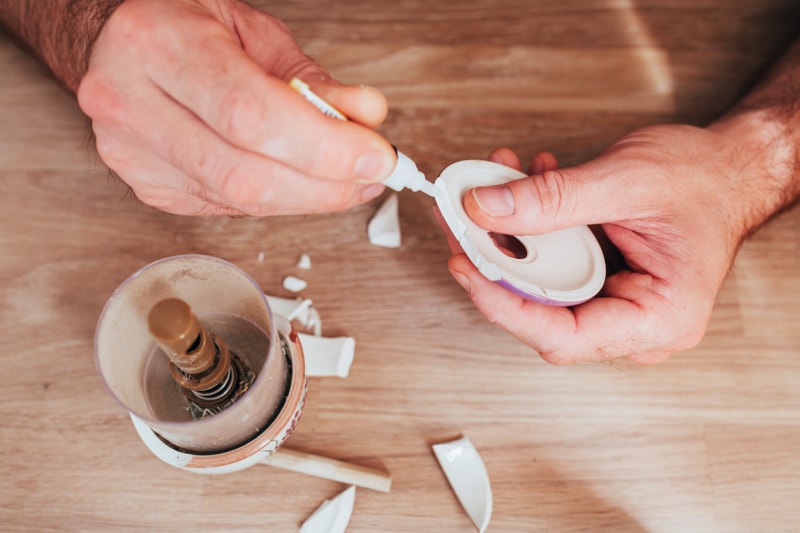 Des mains masculines collent ensemble des fragments de plats en céramique – superglue pour réparer les matériaux durs