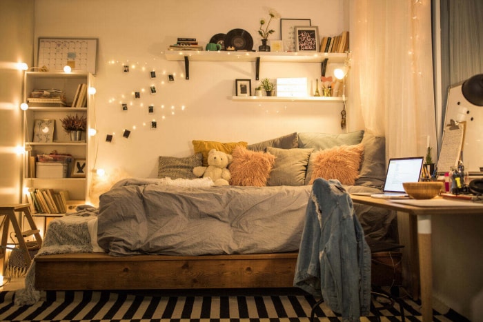 Une guirlande lumineuse sur laquelle sont accrochées des photos est accrochée au mur d'une chambre d'adolescent avec un lit, un bureau et des étagères.