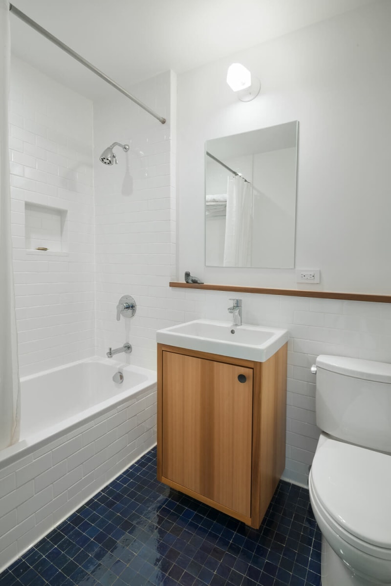 Une salle de bain blanche et bleue avec une étagère en bois intégrée le long du mur du fond.