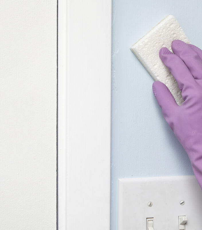 Une femme portant un gant en caoutchouc violet utilise une gomme magique pour essuyer un mur.