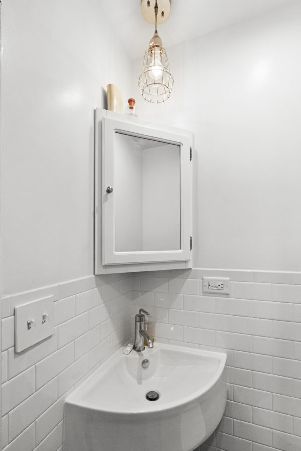 Le coin lumineux d'une salle de bain blanche avec un lavabo d'angle et une armoire à pharmacie.