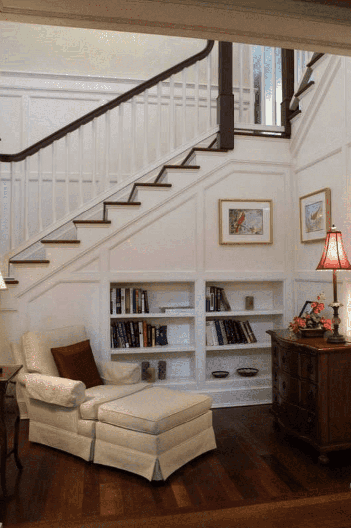 salon majestueux avec chaise blanche et ottoman blanc et escalier blanc avec bibliothèque encastrée en dessous