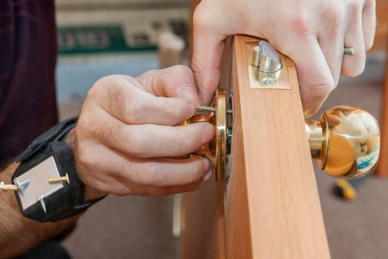 Gros plan d'une personne ajoutant une poignée de porte à une nouvelle porte extérieure. 