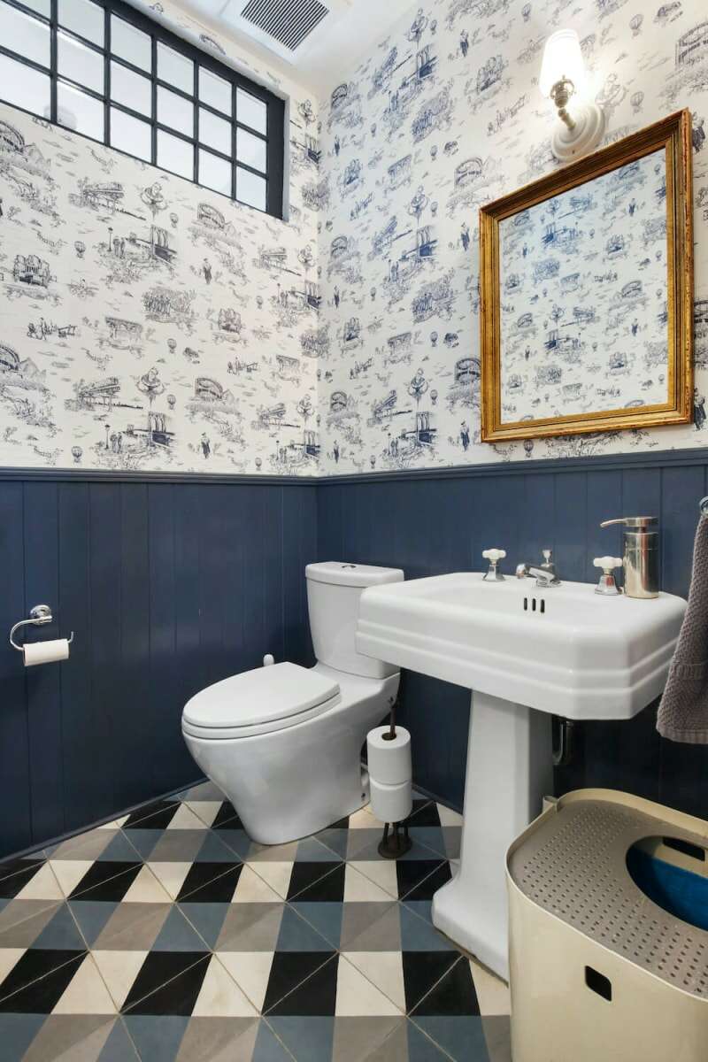 Une petite salle de bain avec des panneaux muraux en bois bleu, du papier peint à motifs blanc et bleu et du carrelage au sol à carreaux bleu et blanc.