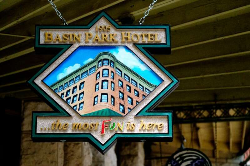 Enseigne en bois sculptée à la main pour le Basin Park Hotel, un bâtiment historique situé au cœur du centre-ville d'Eureka Springs, Arkansas. L'enseigne est suspendue au-dessus du trottoir.