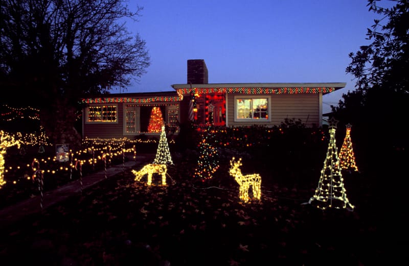 Cour avant d'une petite maison avec des décorations de Noël dans la cour avant au crépuscule, avec des lumières de rennes et d'arbres.