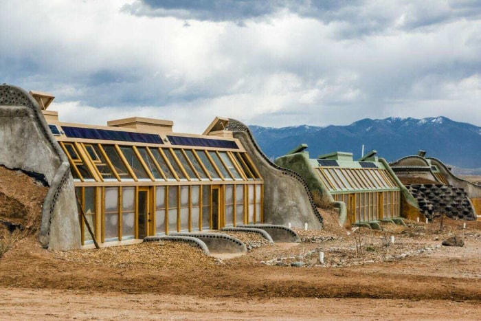 Une rangée de trois maisons earthship se trouve côte à côte dans le paysage désertique du Nouveau-Mexique.